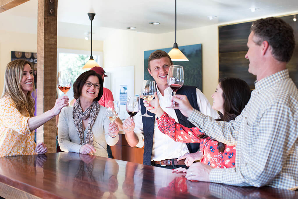 Friends enjoying wine tasting at Scheid Vineyards, California winery, in a cozy indoor setting.