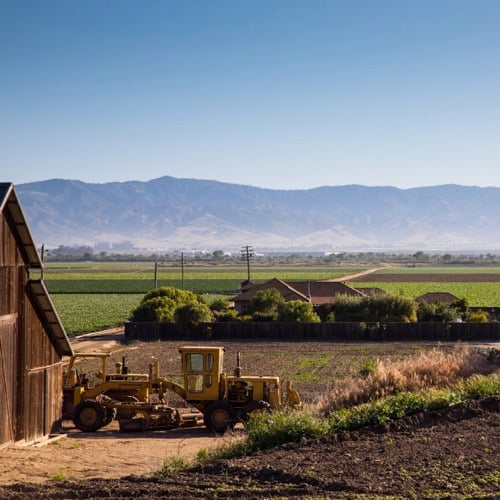 Vineyard landscape with farming equipment and scenic mountain backdrop.