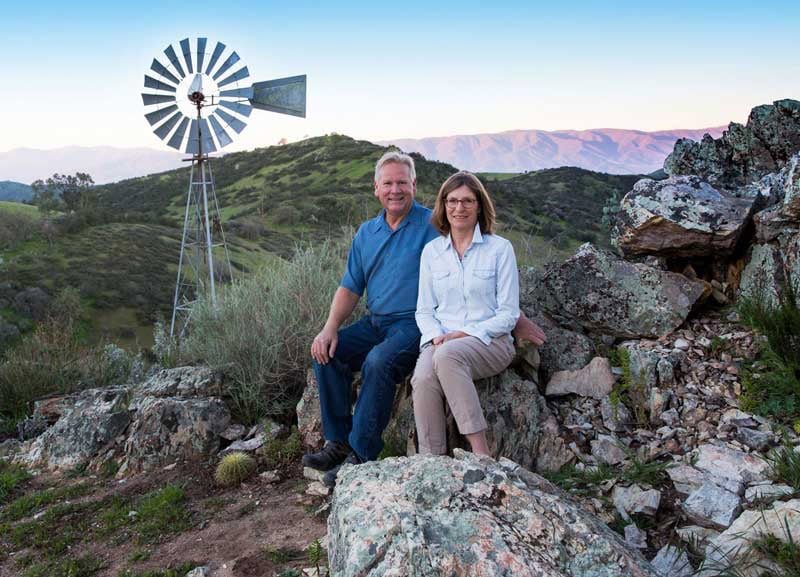 Peaceful vineyard landscape with couple at Scheid Vineyards, lush hills, windmill, California wine country.